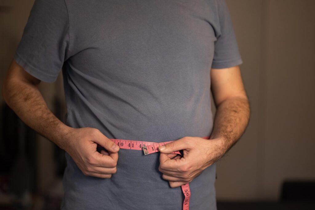 A man in a grey t-shirt measuring his waist