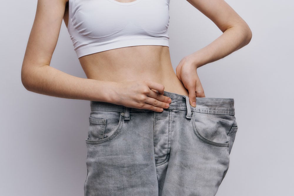 large-pants Woman measuring waist with oversized jeans, weight loss progress, healthy lifestyle.