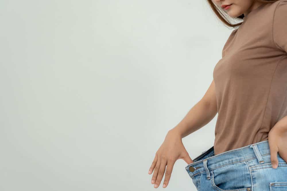 waist-pants Woman measuring waist with oversized jeans, weight loss journey concept.