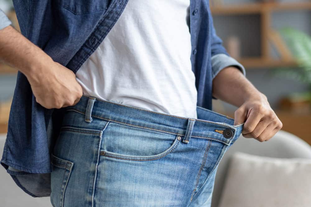 weight-loss-pants Person holding oversized jeans to show weight loss progress at Prescription Weight Loss clinic.