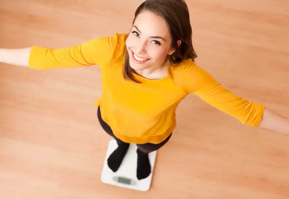 Weight Loss Treatment_Fort Lauderdale Happy woman standing on a scale, celebrating weight loss success.