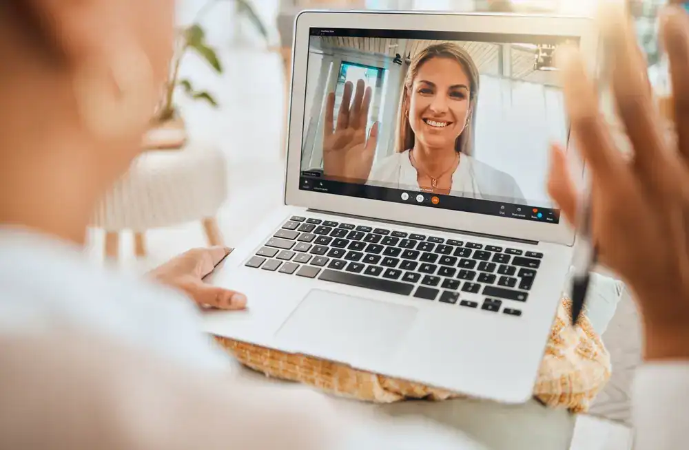 Weight Loss Treatment_Fort Myers (2) Woman on video call smiling and waving on laptop screen for weight loss consultation.