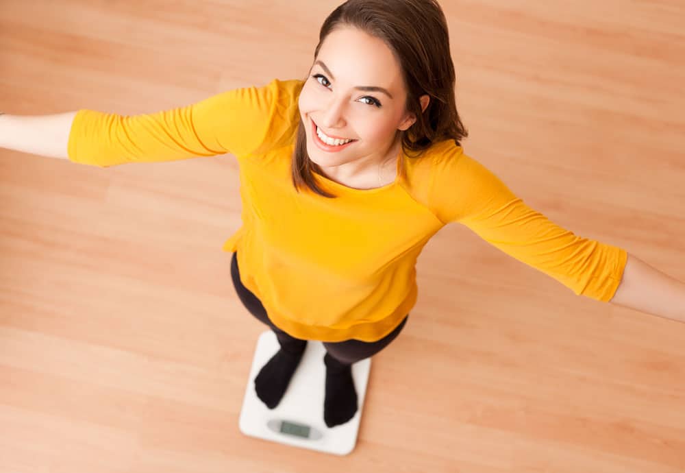 Happy Woman on Scale for Weight Loss Woman smiling on scale, celebrating weight loss success.
