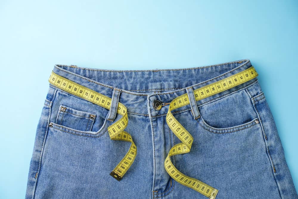 Weight Loss Jeans and Measuring Tape Blue jeans with a yellow measuring tape for weight loss measurement.