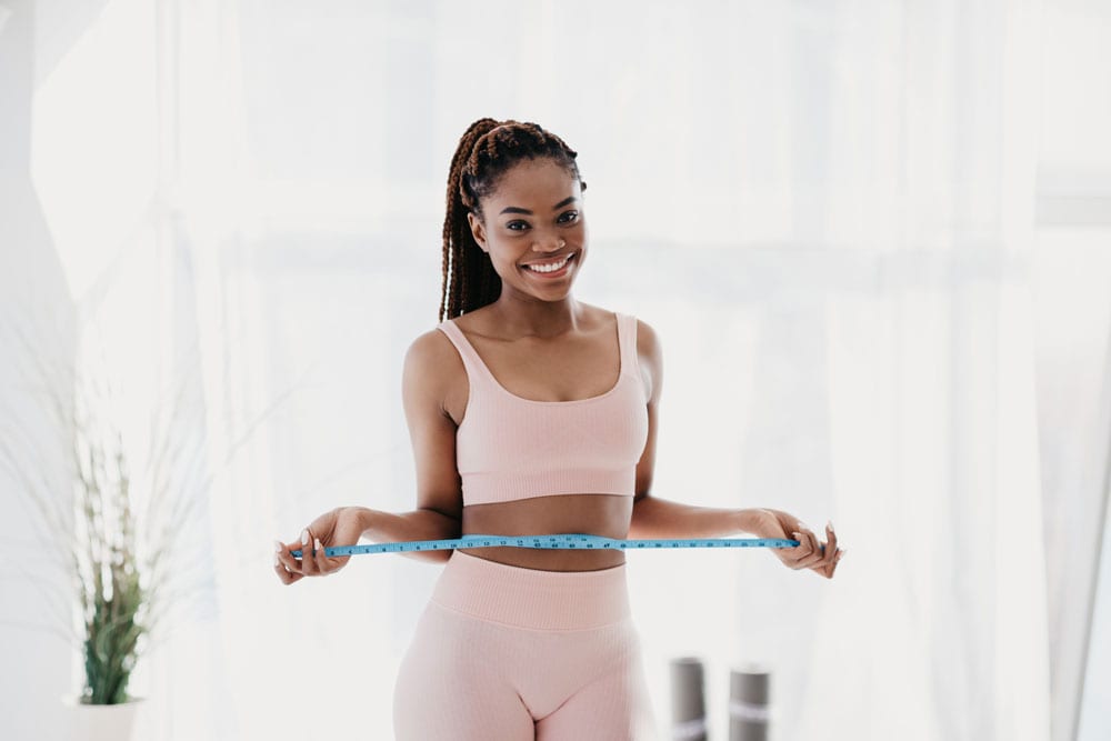 Smiling woman measuring her waist with a tape measure for weight loss.