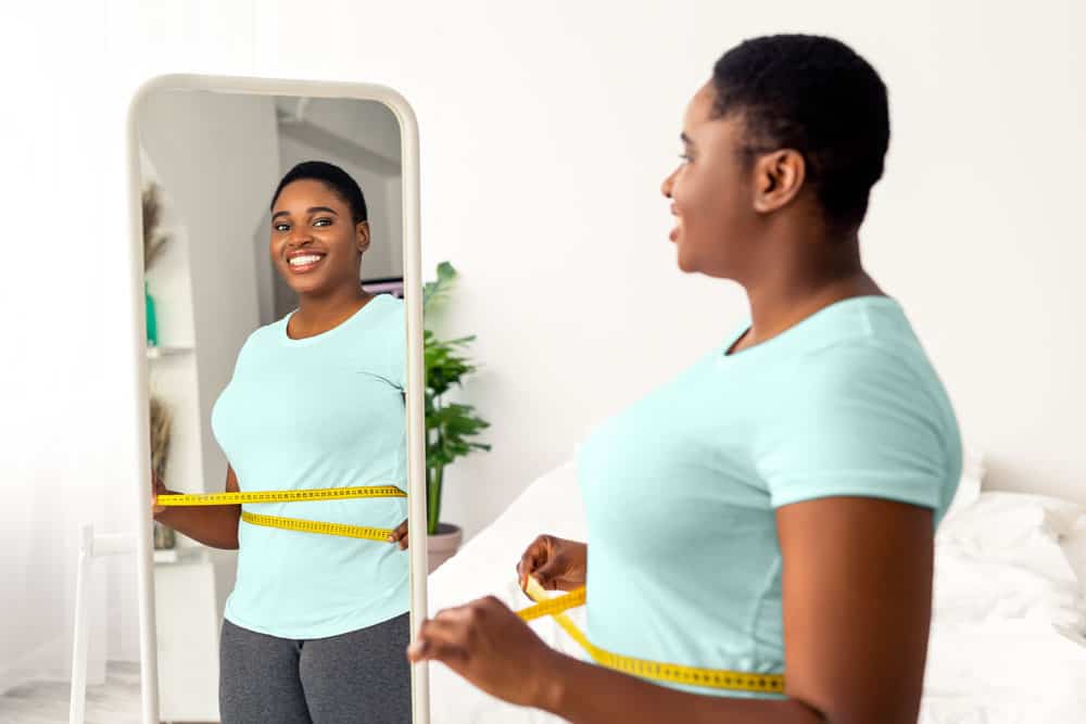 Woman measuring her waist in front of a mirror for weight loss progress.