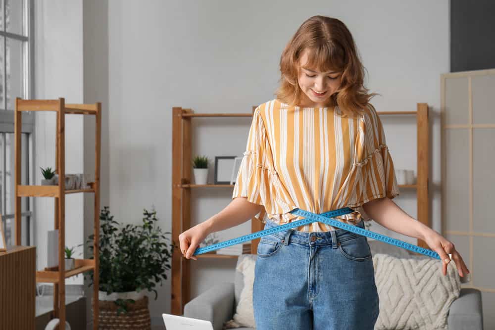 Woman Measuring Waist for Weight Loss Woman measuring her waist with a tape measure for weight loss progress.